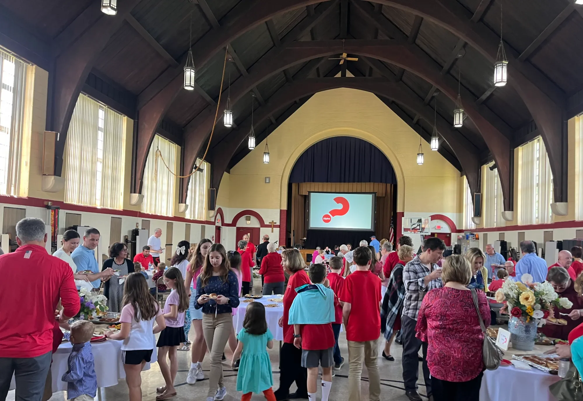 A large room of people with tables of food and a screen at the front